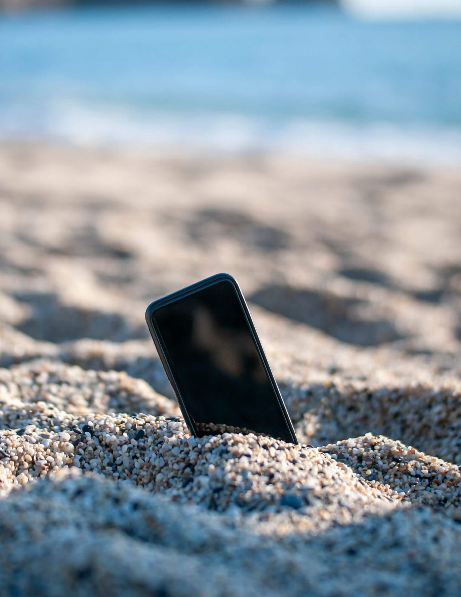 A smart phone sticking out of the sand at the beach