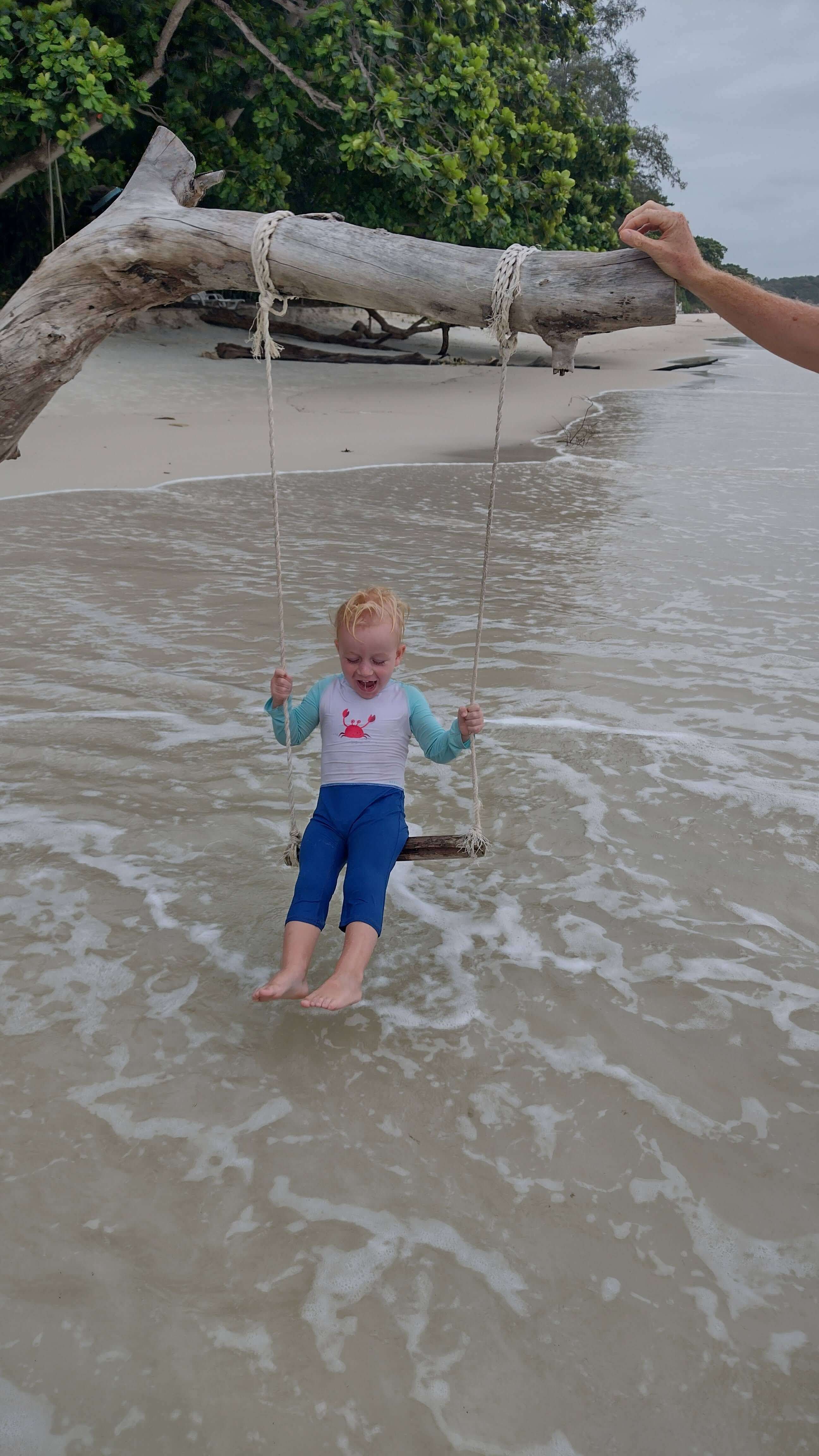 A white toddler playing on a swing at the beach