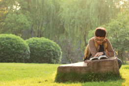 A man sitting in a green space reading a book
