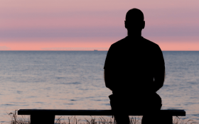 The silhouette of a man sitting alone in front of the ocean at sunset