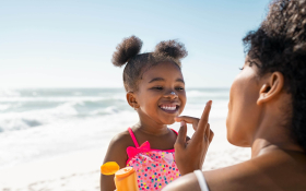 A Black woman applying sunscreen to the face of her daughter at the beach