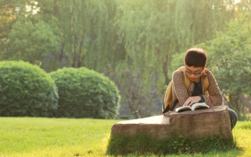 A man sitting in a green space reading a book
