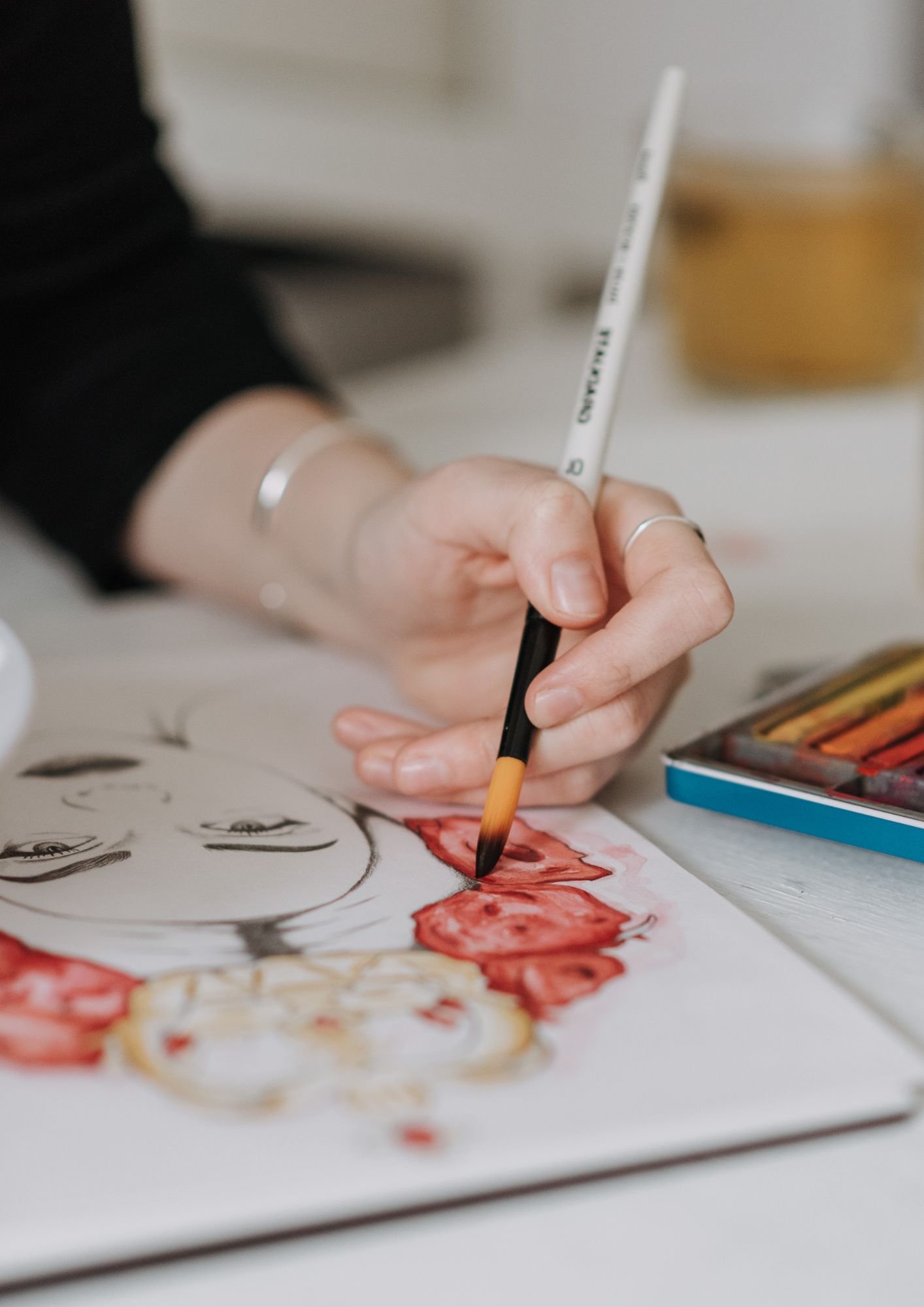A white person holds a paintbrush and works on a painting 