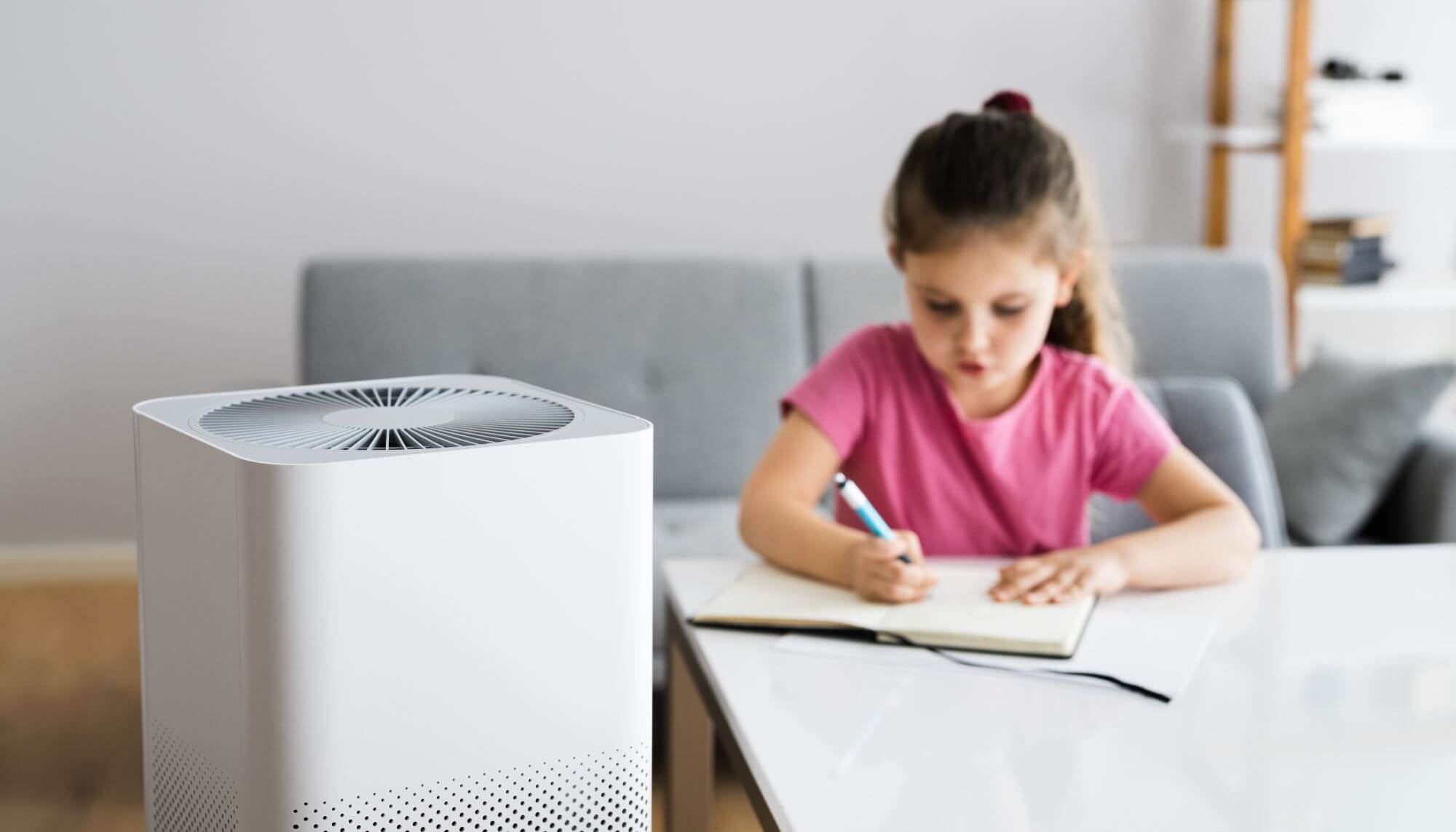 An indoor air purifier next to a young girl working at a desk.