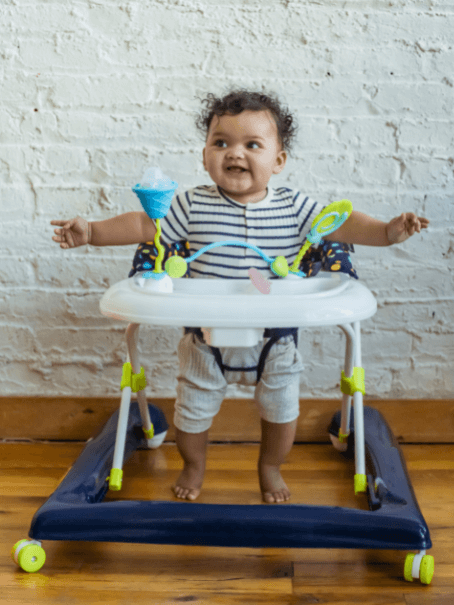 A Black baby standing in a baby walker and smiling 