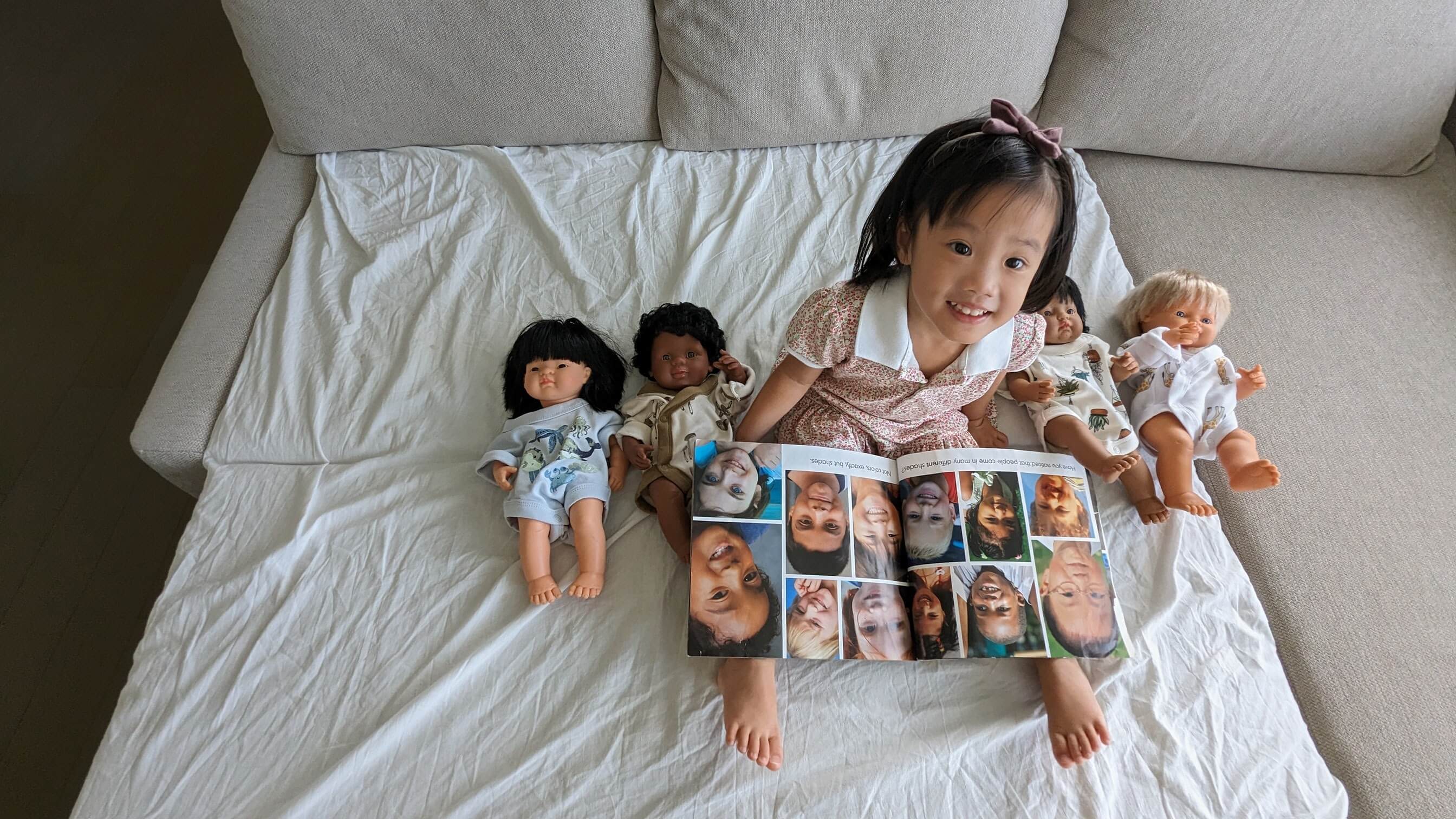 A two-year-old Chinese Australian girl reading a book about racial diversity and playing with a group of racially diverse dolls. 