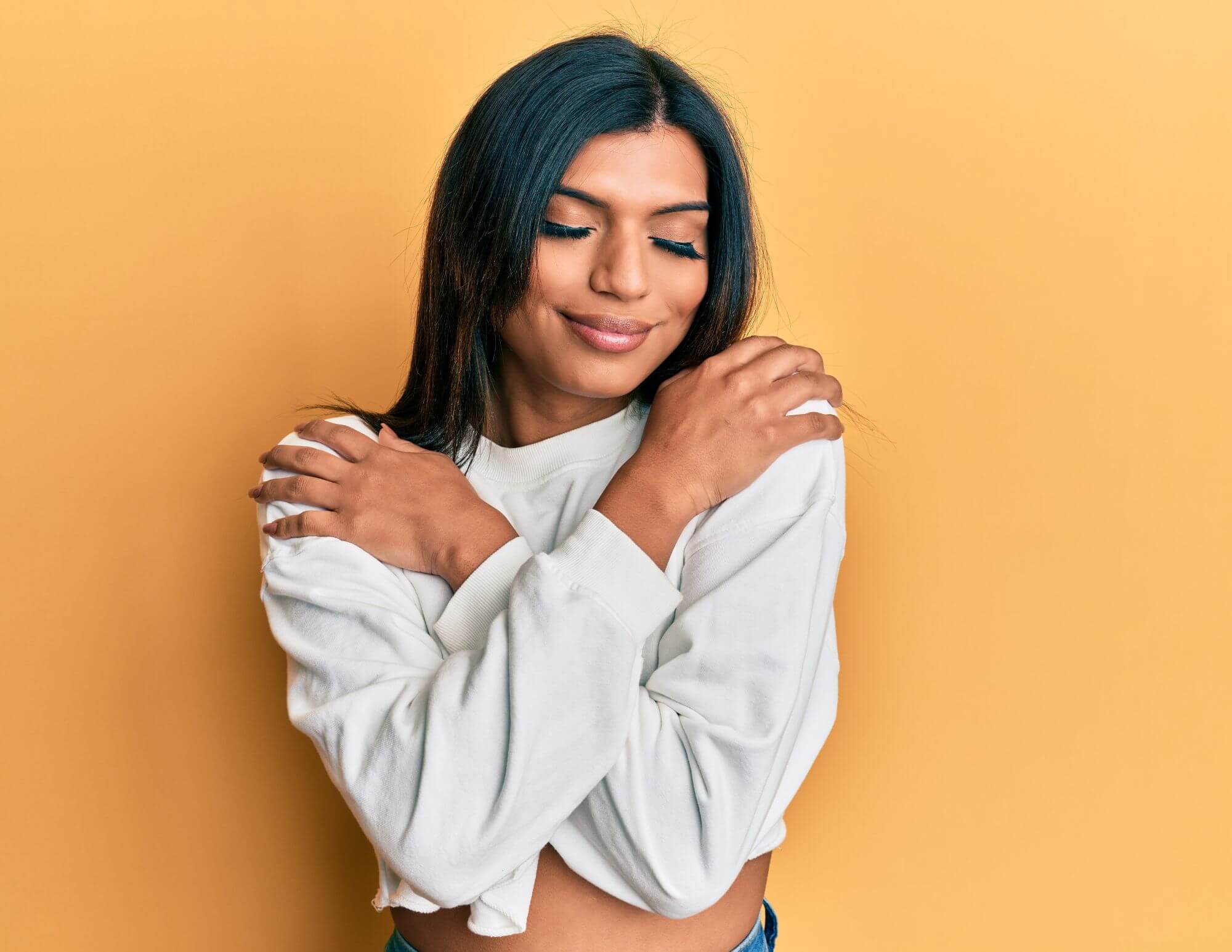A South Asian woman hugging herself with her eyes closed and smiling