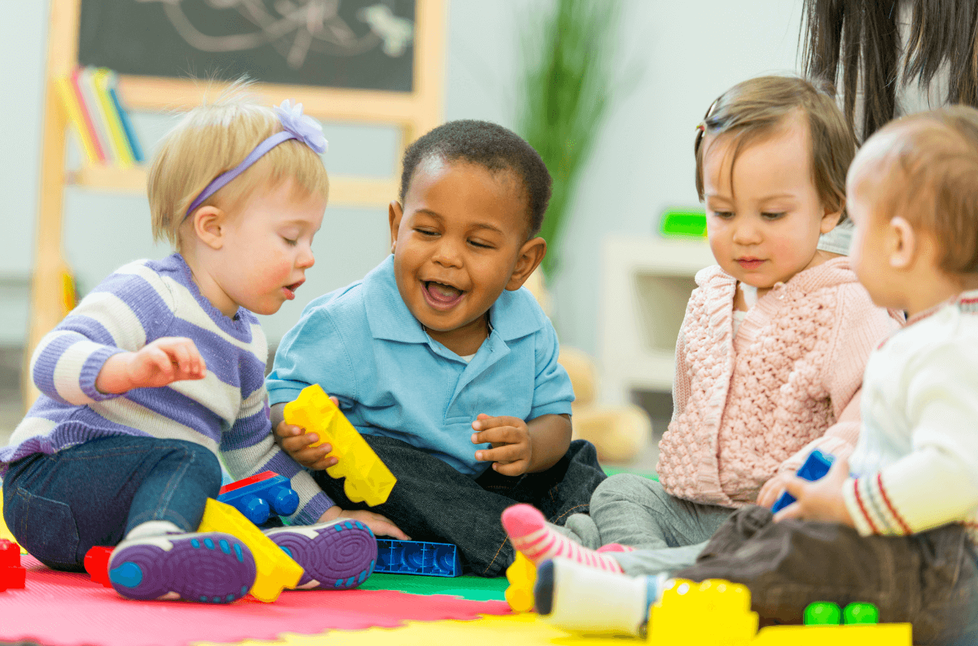 A multiracial group of young toddlers sitting on the floor together and playing with blocks