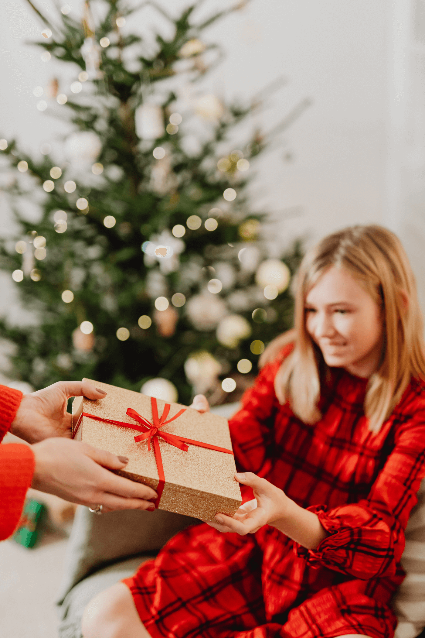 A girl in red accepts a Christmas gift in front of a Christmas tree