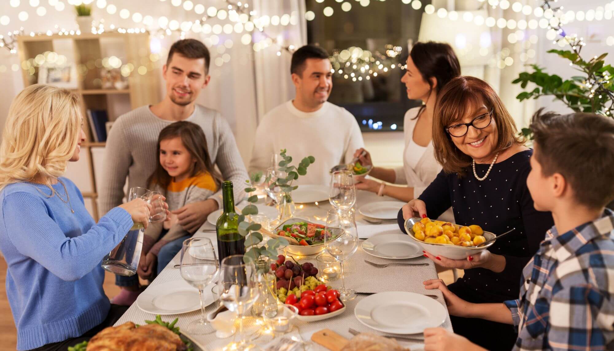 A group of adults and children seated around a table sharing a meal.
