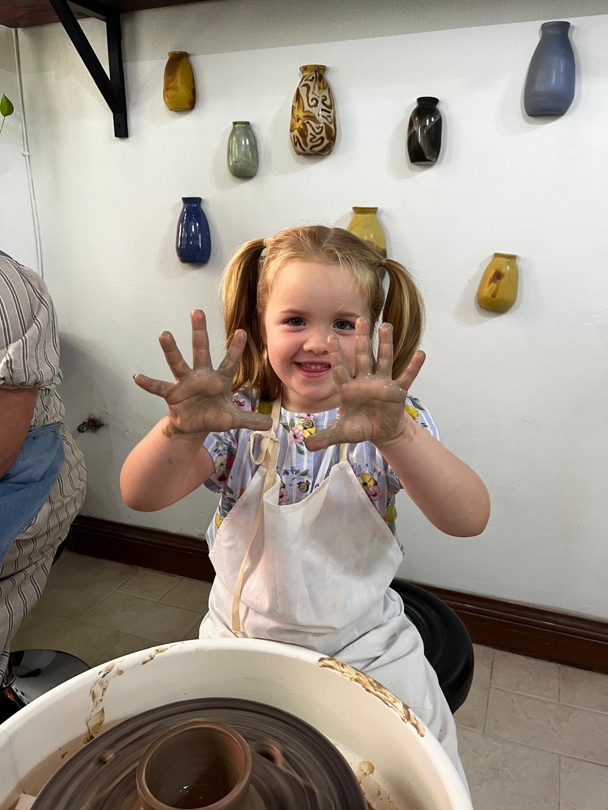 A girl raises clay covered hands
