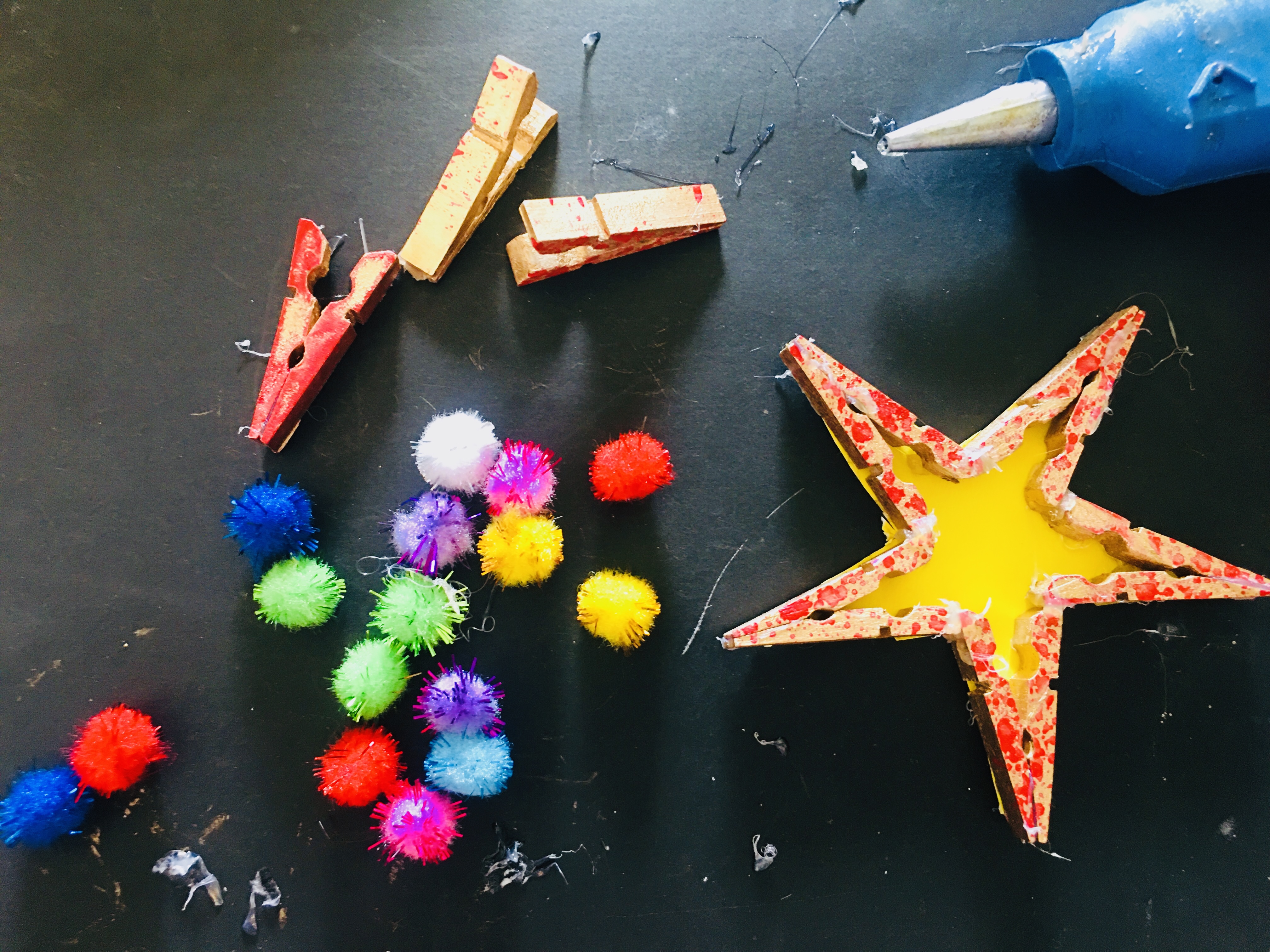 A clothespin star, pompoms and a glue gun on a table.