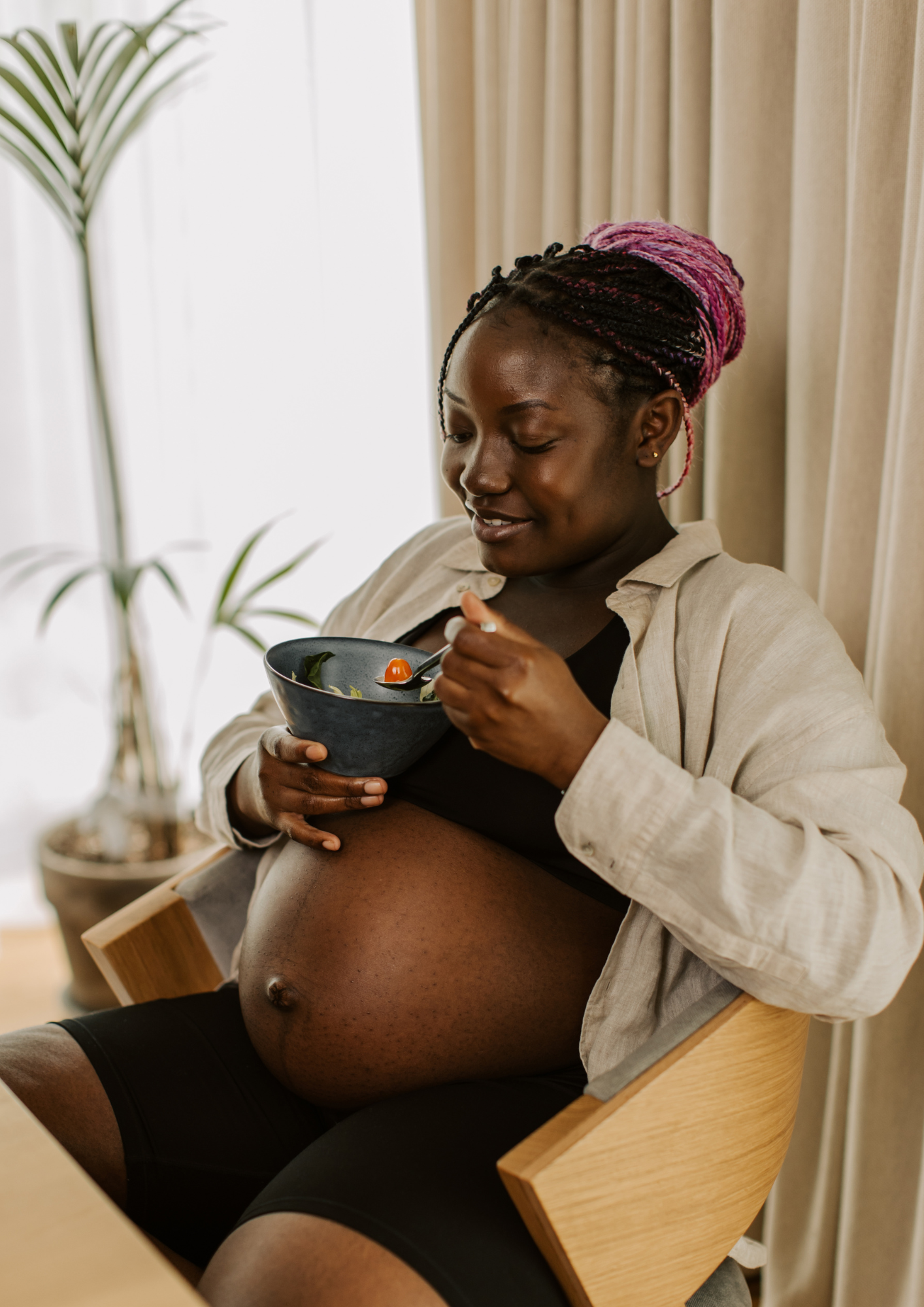 A pregnant Black woman eats a bowl of salad
