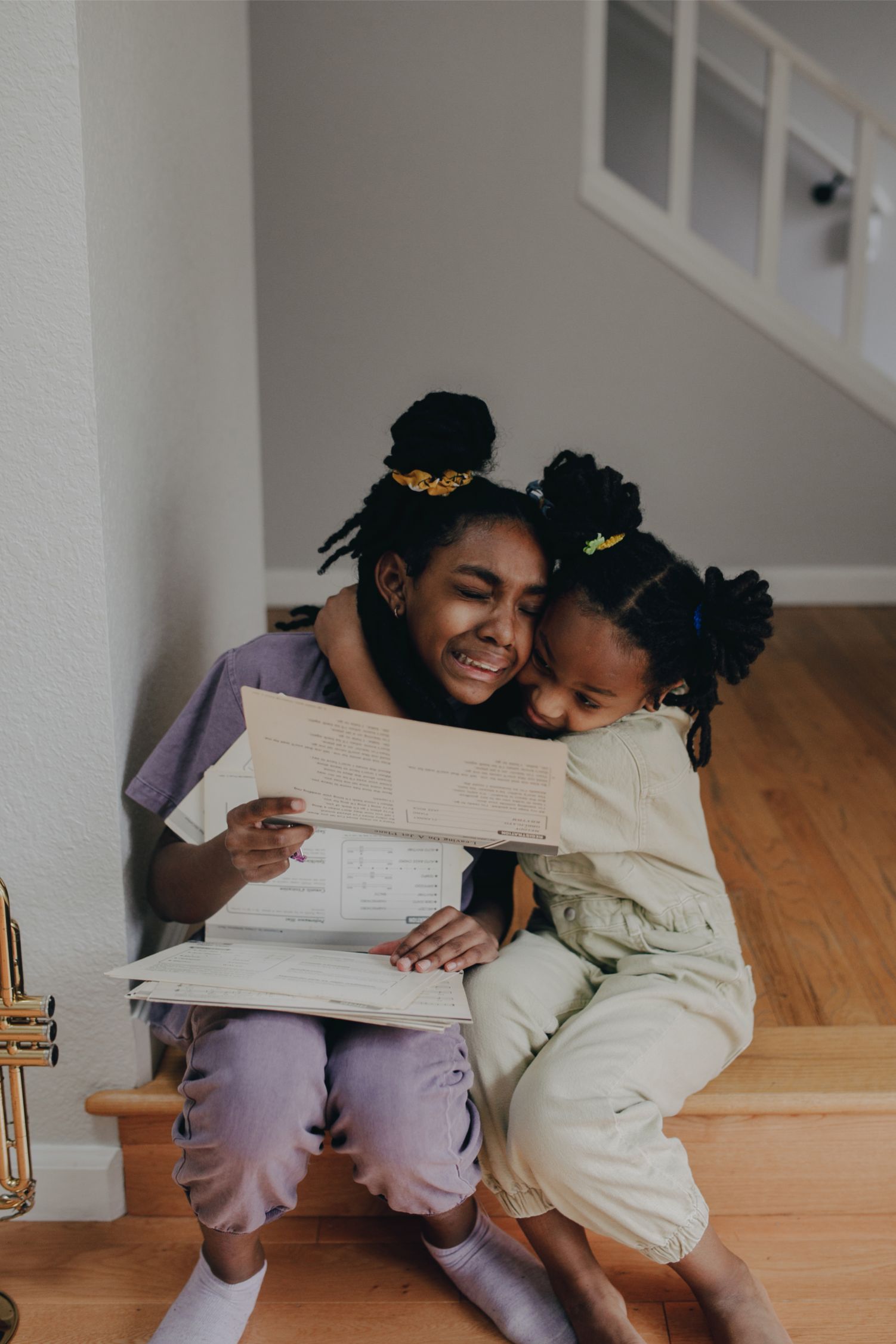Two crying sisters hug each other while sitting on the stairs