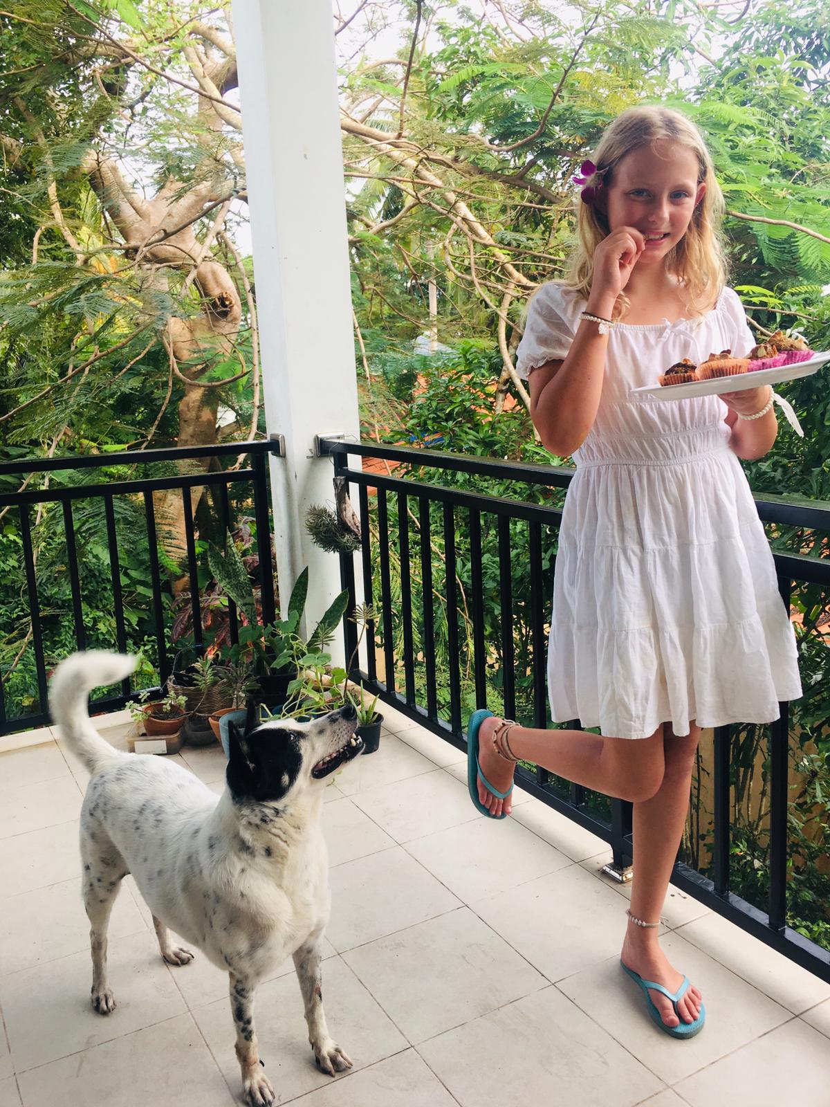 A white girl holds a plate of freshly baked oat and banana muffins as a black and white dog looks on