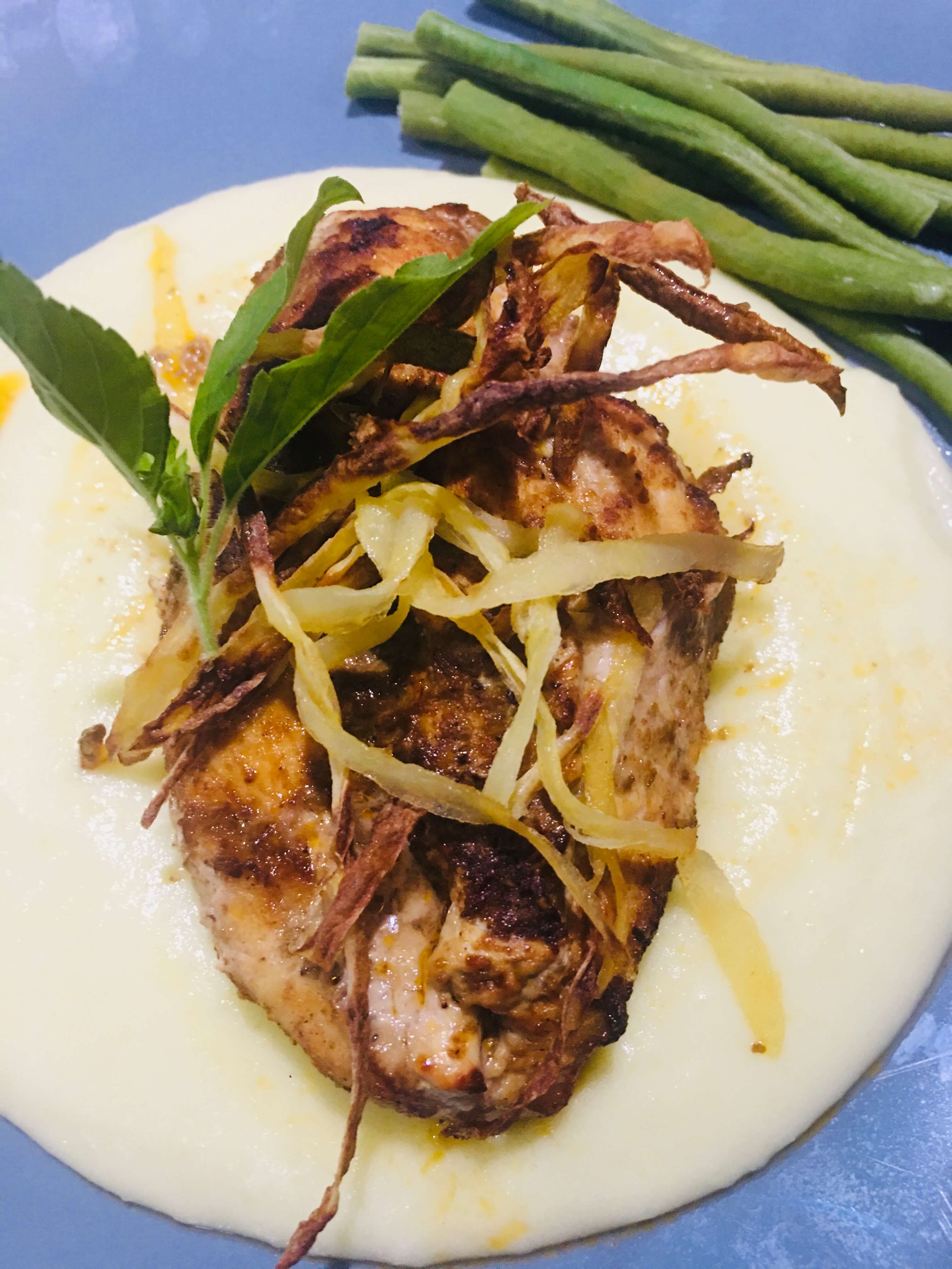 A dish of air-fried chicken breast on a bed of mashed potato and a side of green beans