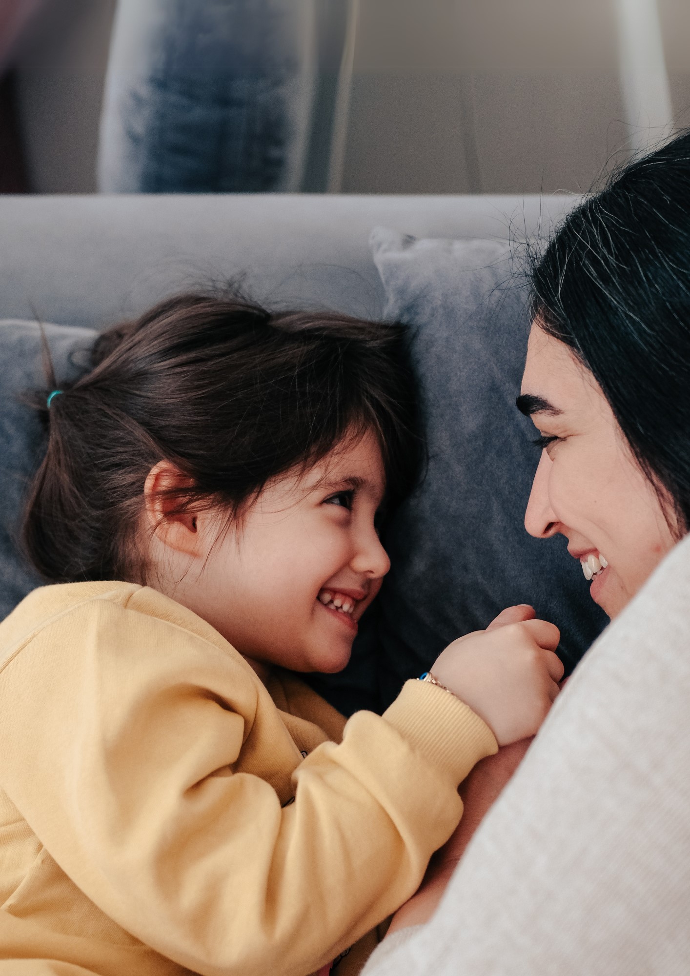 A mother and daughter lie facing each other on a couch.