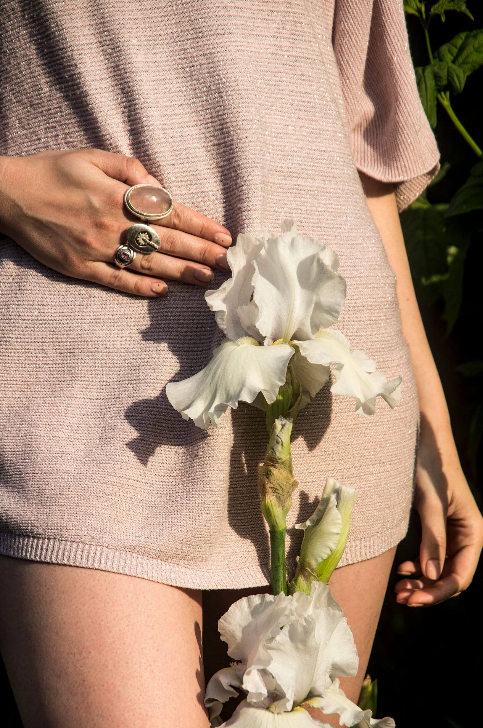A close up of a woman's abdominal and pelvic regions. The woman is wearing an oversize beige knitted top. A white flower extends upwards from the bottom of the frame to where her uterus would be.