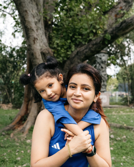 A mother and daughter hug in front of a tree
