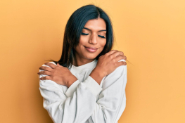 A South Asian woman hugging herself with her eyes closed and smiling
