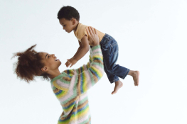 A Black woman lifting her son above her head by holding him under his armpits