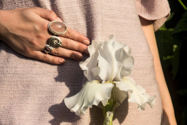 A close-up of a woman's pelvic region. She is dressed in a beige top and is holding a white flower in front of her in line with her uterus