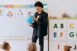 A teacher holds a globe at the front of a classroom