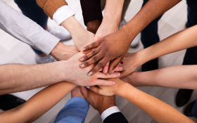 Many hands - each one a different skin tone to the rest - placed on top of one another. 