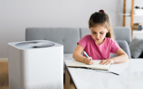 An indoor air purifier next to a young girl working at a desk.