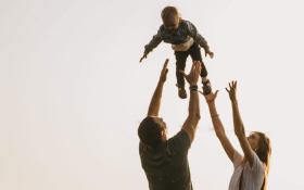 A mother and father playing and throwing their toddler into the air