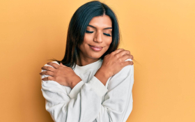 A South Asian woman hugging herself with her eyes closed and smiling
