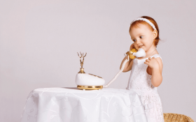 A redheaded toddler girl pretending to talk on an ornate white and fold telephone