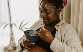 A pregnant Black woman eats a bowl of salad