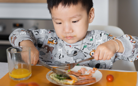 An Asian toddler eats a plate of food