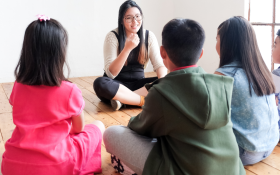 A teacher and small group of children gathered in a circle on the floor