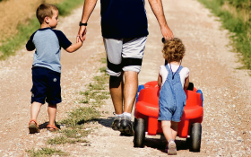 A dad and two boys walk away from us holding hands