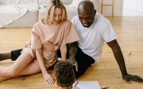 A couple sit on the floor facing their child