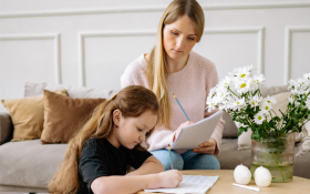 A child writes whilst an adult watches them.