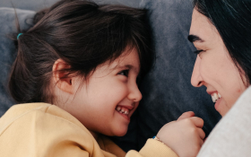 A mother and daughter lie facing each other on a couch.