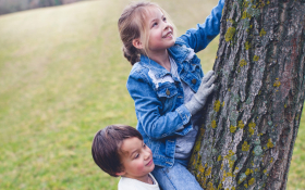 A child climbs a tree with the help of a friend. 