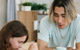 A teenager talks to his sister at the kitchen table