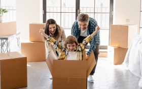 Two parents push their joyful child in a cardboard box.