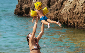 A mother in the sea throws her child in the air.