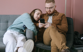 A couple sit on a couch looking at their phones