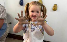 A girl raises clay covered hands